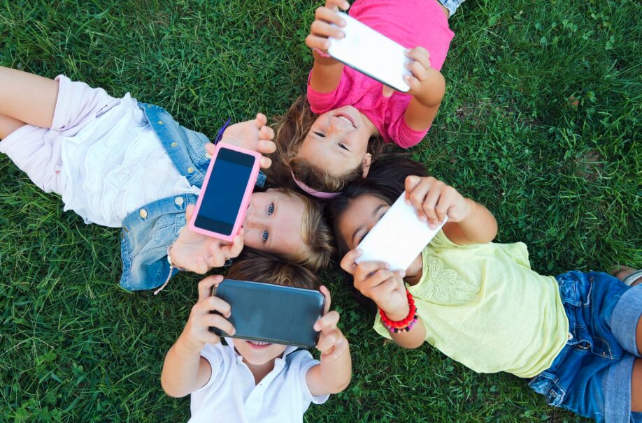 Children laying on grass looking at smartphones