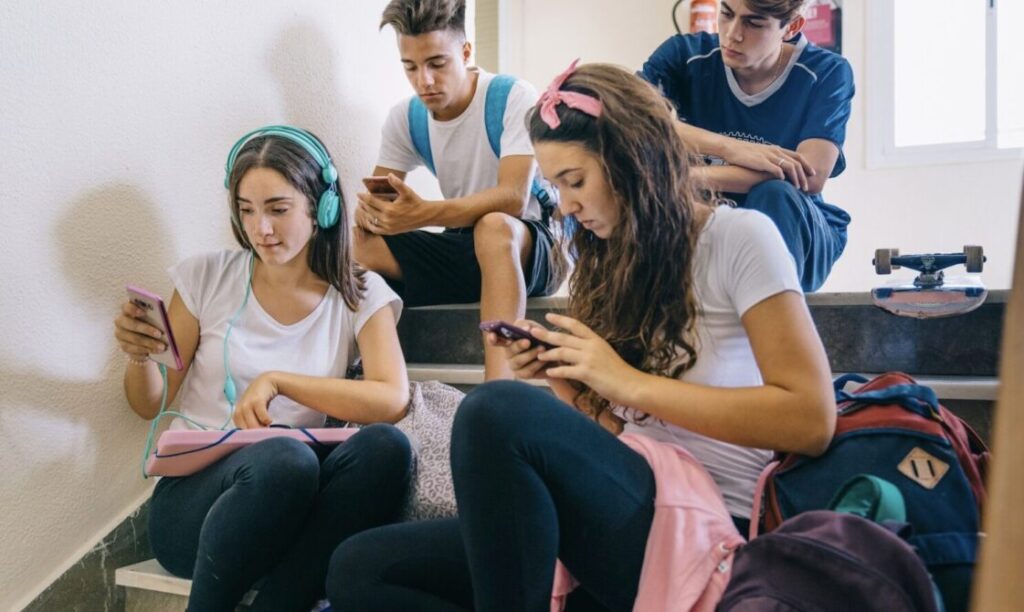 Teenagers sitting in school and checking their smartphones