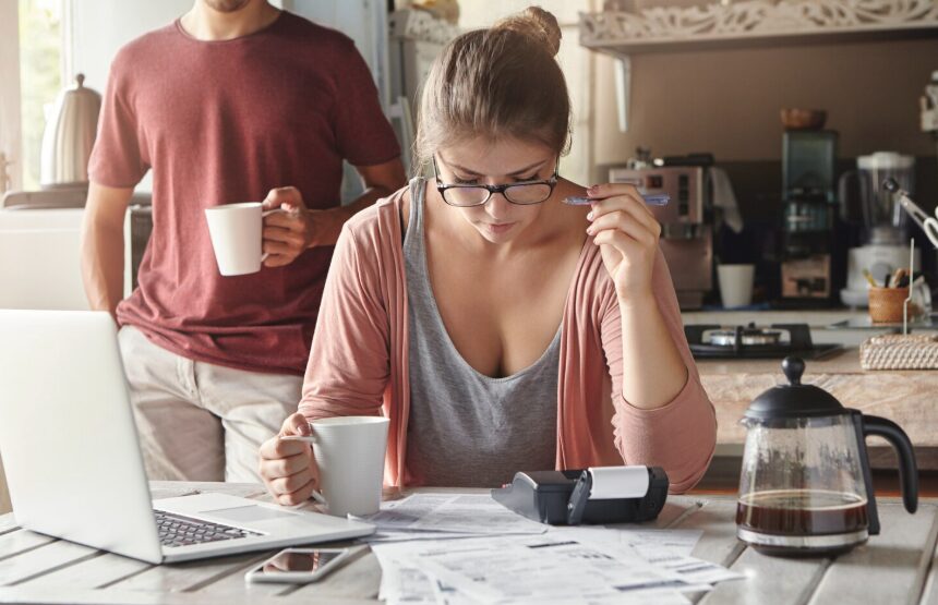 A young woman sitting in the kitchen and checking her expenses with a calculator