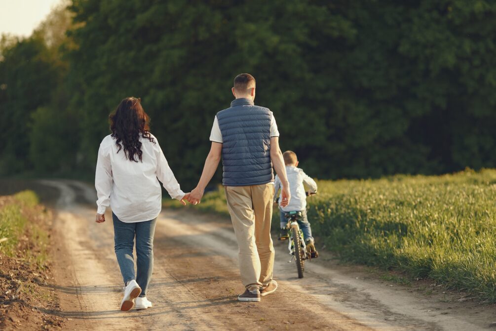 Parents holding hands and walking besides a little boy on a bycicle