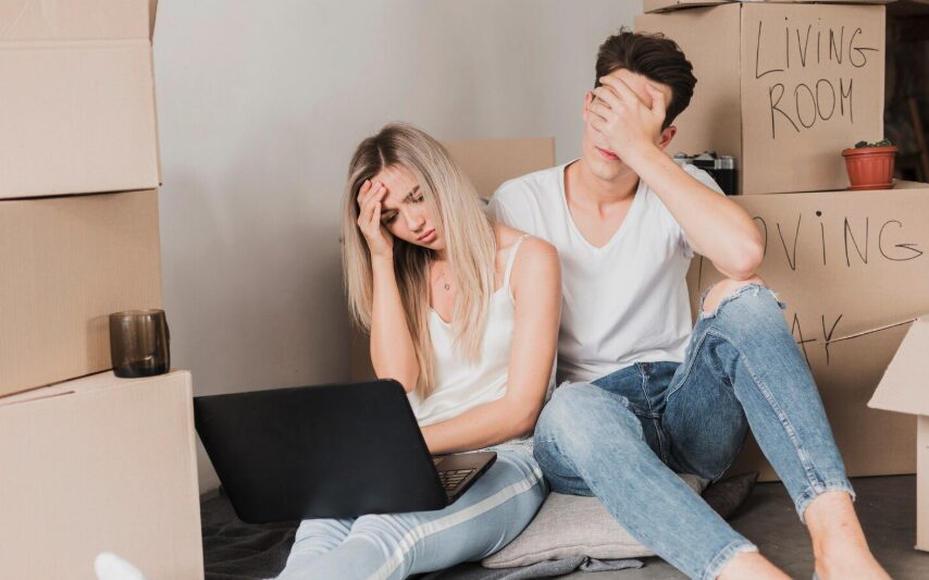 A young couple surrounded with boxes feeling stressed because of the housing crisis.