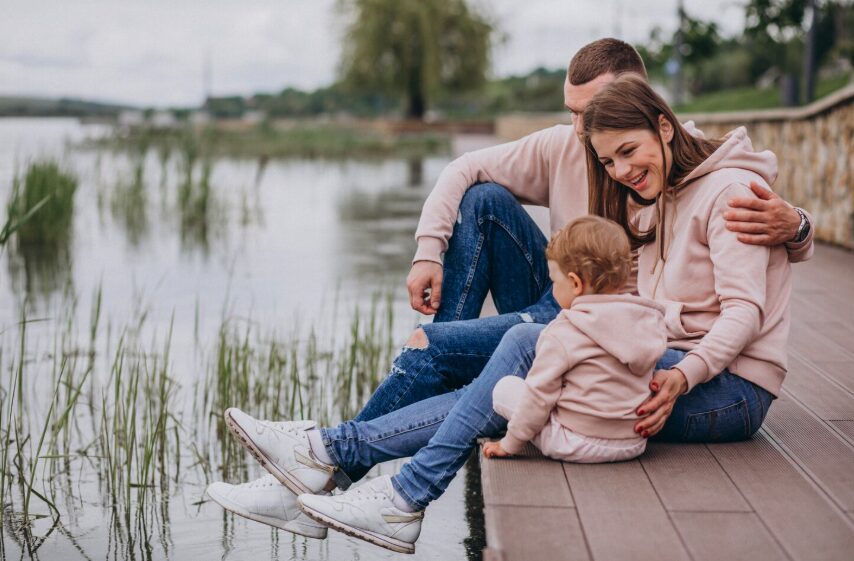 A young family sitting beside a lake.