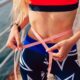 Young sportswoman measuring sizes her body with tape after workout