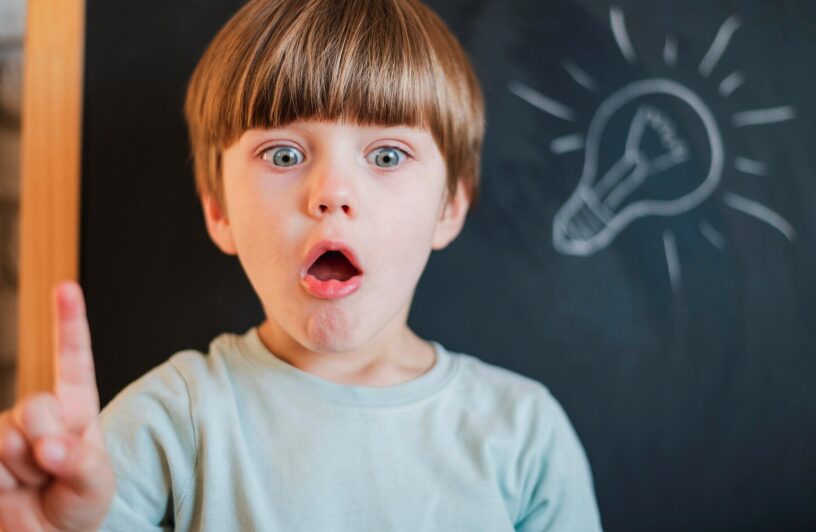 A child with pointing finger up and a lightbulb drawn on the board behind him.