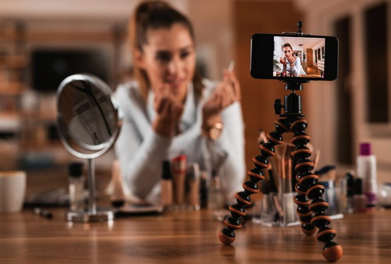 A woman influencer filming herself while showing make up on her phone.