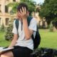 A boy sitting in front of a university holding his head tired of reading a book