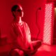Young woman sitting on the floor using a red light therapy panel