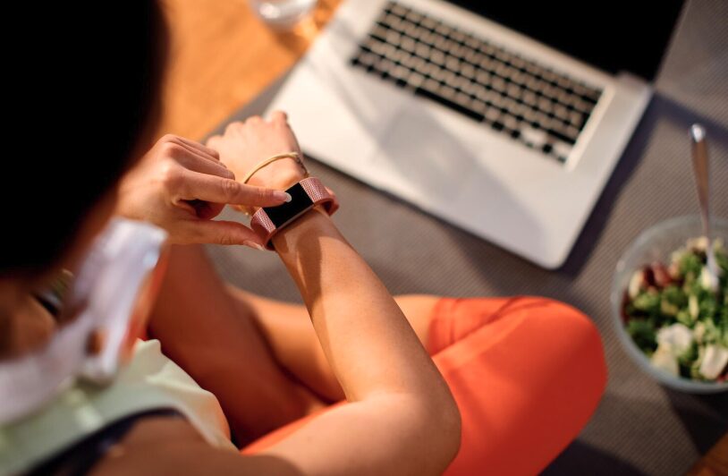 A woman watching her smart watch over a laptop and a bowl of salad.
