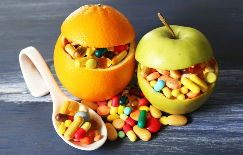 An orange and an apple fulled with colorful supplements.