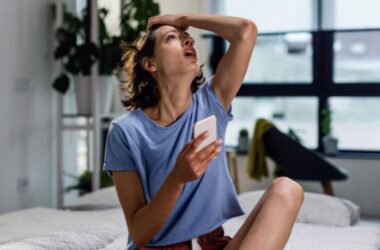 Young woman sitting on a bed feeling exhausted by optimizing her health.