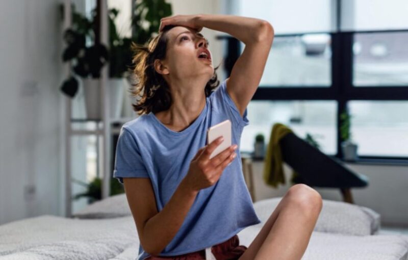 Young woman sitting on a bed feeling exhausted by optimizing her health.
