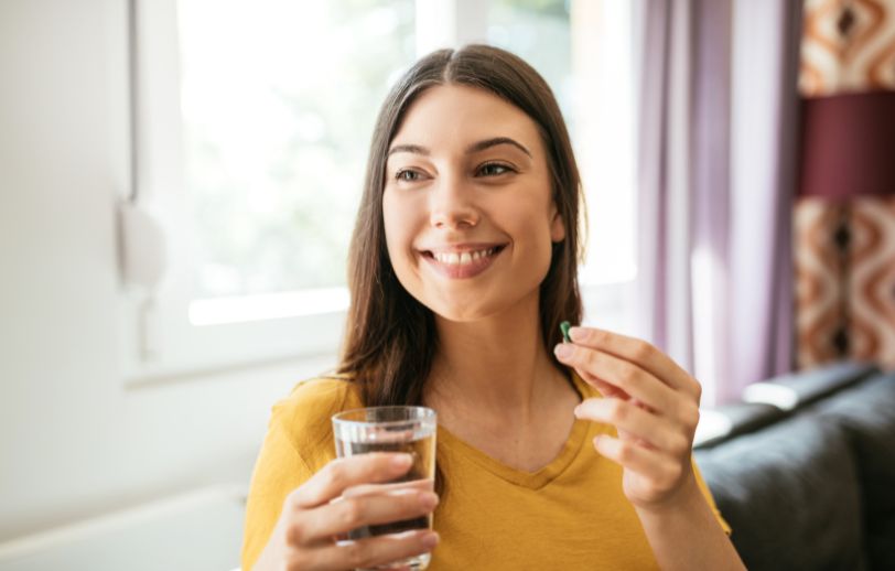 Woman holding a capsule and a glass of water.